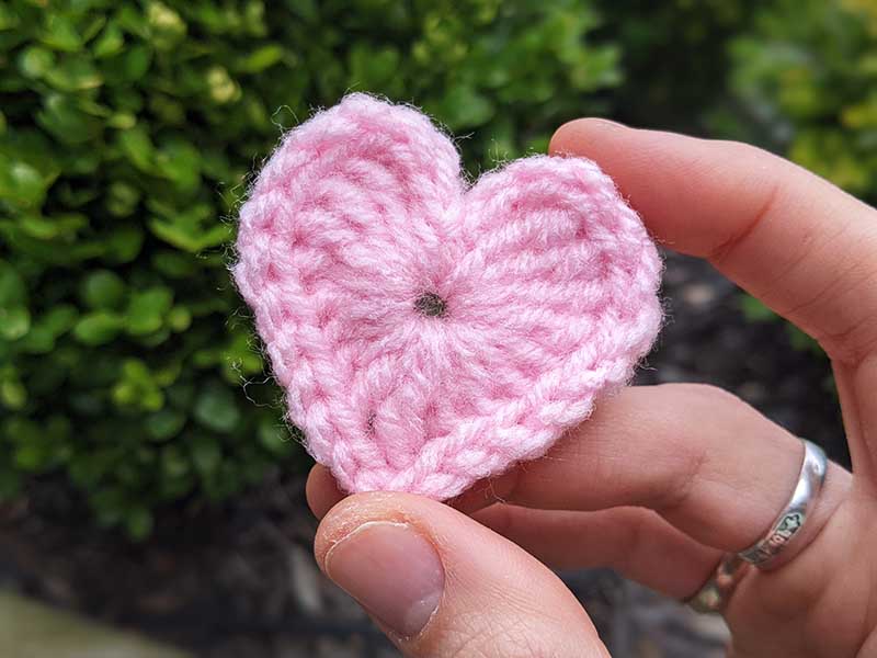 close up shot of a pink crochet heart on the green background