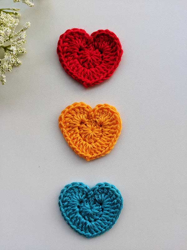 three crochet solid decor hearts - one red, one blue, and one yellow