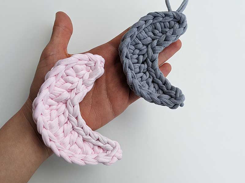 two crochet crescent moons made with pink and gray yarn