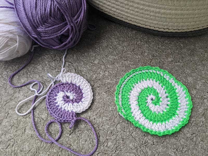 two crochet spiral hot pads - violet & white one is work-in-progress and green & white one is finished