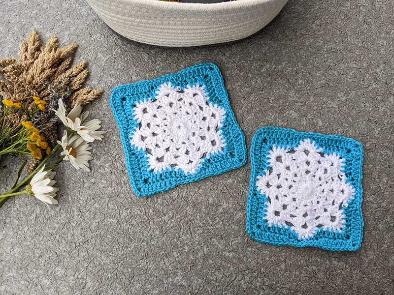 two crochet granny squares with Christmas-style white snowflake in the middle and frosty blue border