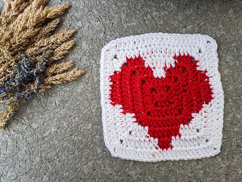 crochet granny square pattern with red heart in the middle and white canvas