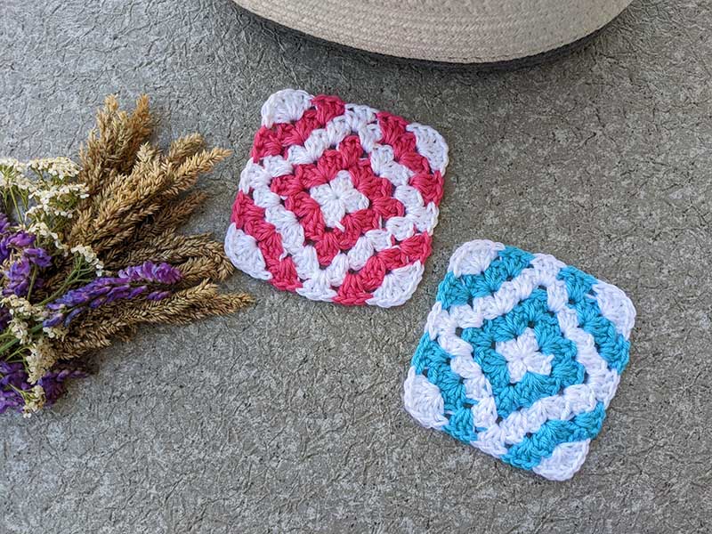 two crochet granny squares - one with a red diamond and another one with blue diamond in the middle