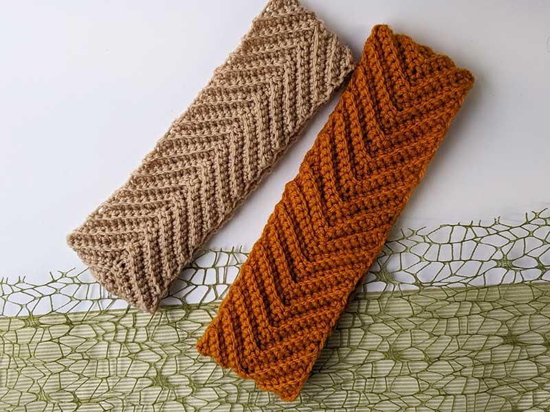 two single crochet chevron ear warmers laying next to each other - one has orange color and another one has latte color