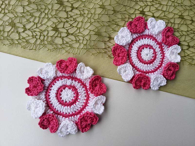two crochet coasters with decor hearts made with white and raspberry color yarn