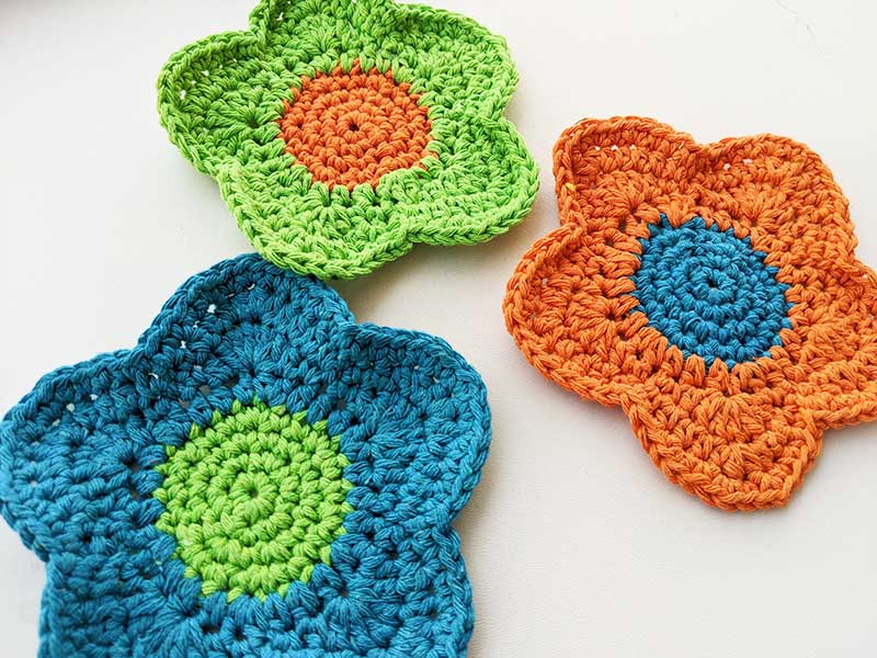 three crochet flower hot pads made in different colors