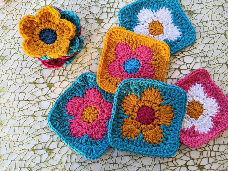 five crochet daisy granny squares made in different colors laying next to each other