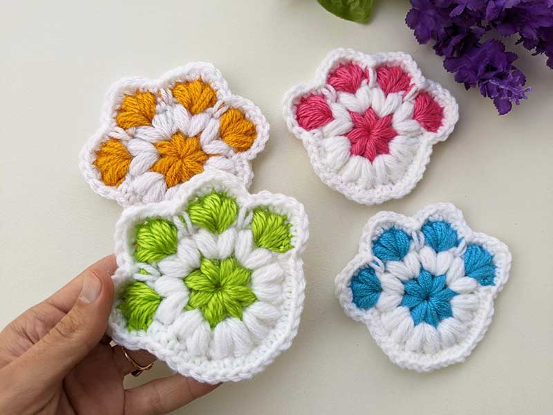 four crochet paw print coasters made in different colors - green, orange, red, and blue