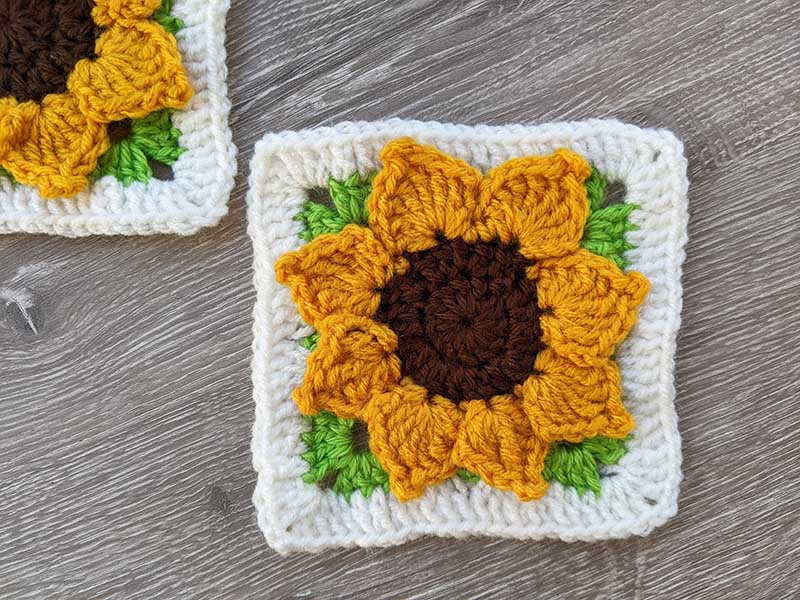 a three-dimensional crochet sunflower granny square made in four colors - brown, yellow, green, and white