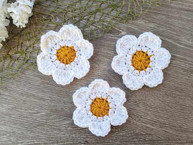 three crochet 6 petal daisy flowers arranged in a triangle