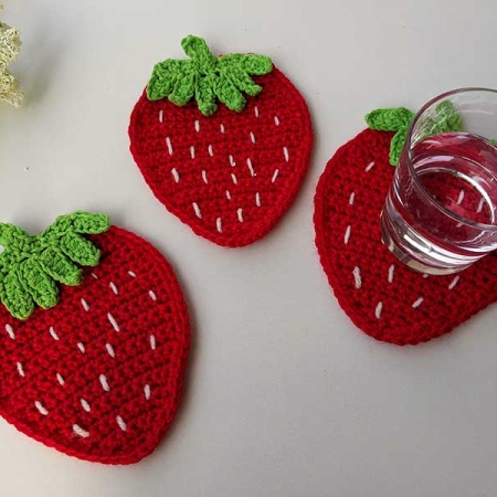 three crochet strawberry coasters next to each other with a glass of water on one of them