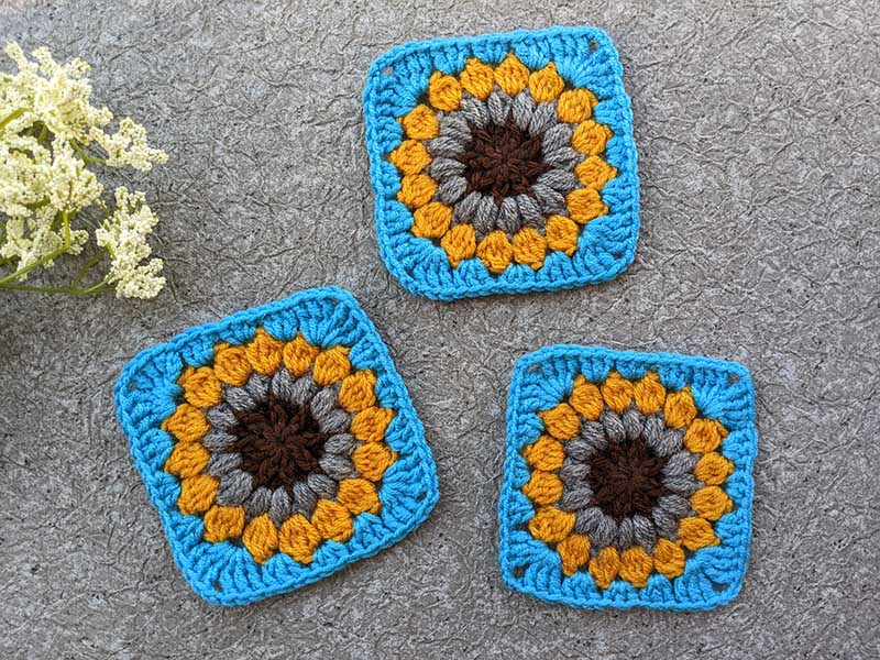 three four-color sunburst granny squares - brown and gray middle, yellow leaves, and blue edge