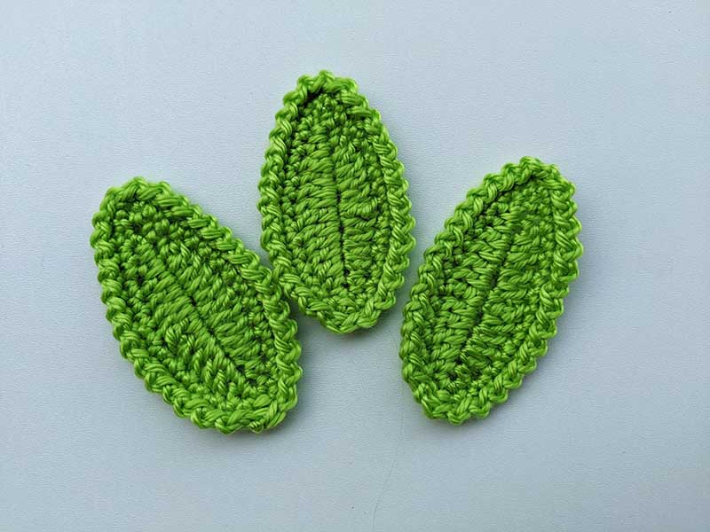 three crochet oval leaves made with green yarn on white background
