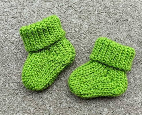 two crochet baby booties arranged to mimic a baby step