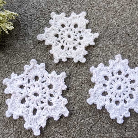 three crochet lace snowflakes arranged in a triangle shape - one at the top and two at the bottom
