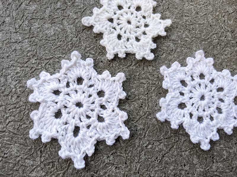 close up view of three crochet lace snowflakes