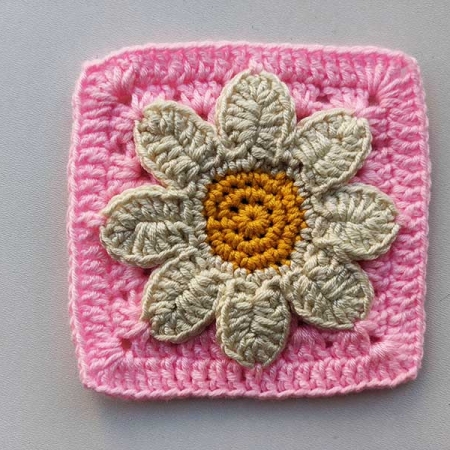 crochet 3-D daisy granny square with pink base, white petals, and yellow bud
