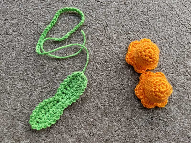 assembly parts of the crochet flower bells - two orange bells, green leaves and yarn hook