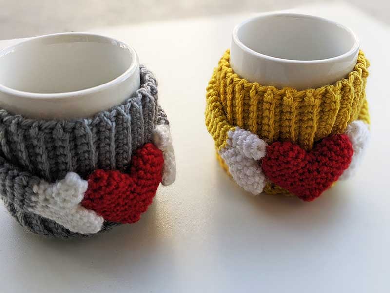 two crochet cup cozies with hearts shown on mugs